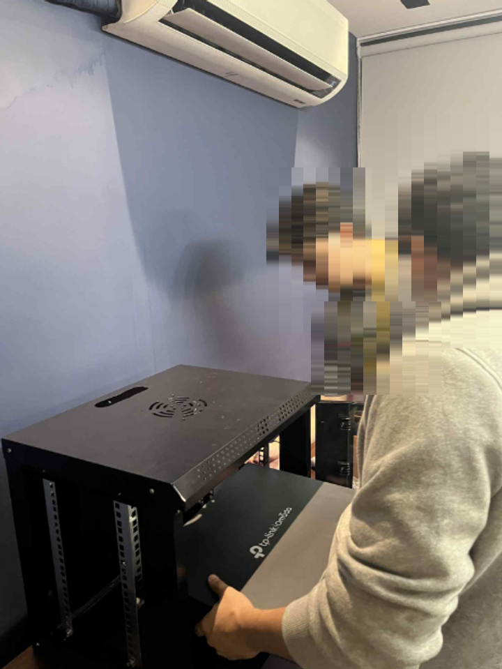 Two team members mounting network equipment into a wall-mounted rack enclosure on site. Faces are masked.